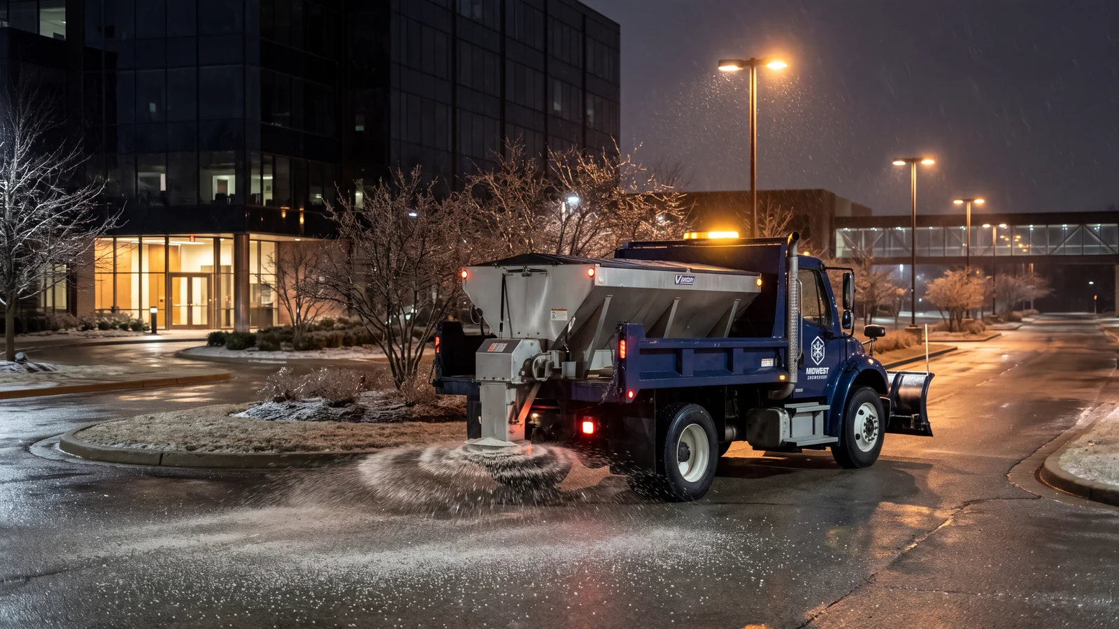 A custom brand scene of a Midwest Freightliner spreading granular salt on a private office campus drive at night.